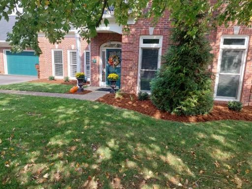 A brick house with a green door and teal garage door. Yellow mums and a pumpkin decorate the front yard.