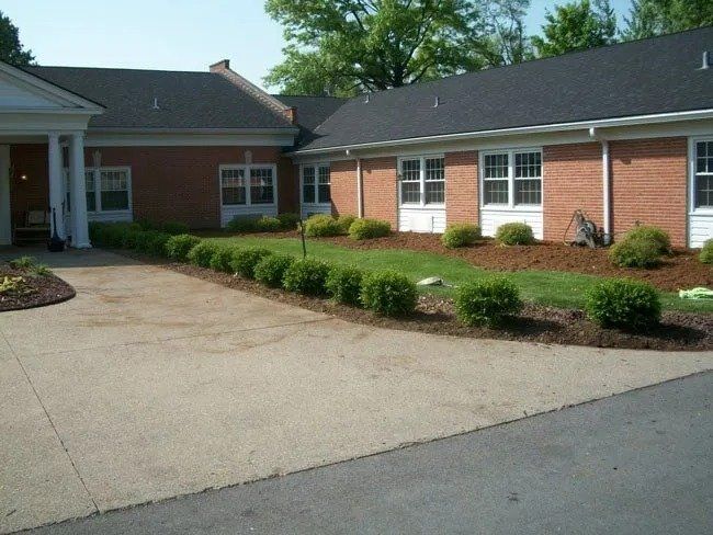 Exterior view of a brick building with a concrete driveway and a row of green shrubs.