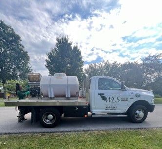 White pickup truck with a water tank on a flatbed, parked on a street. The truck has a company logo on the door.