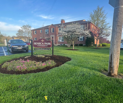 Seneca Park apartment complex with a sign, a car, and a tree with white blossoms, on a green lawn.