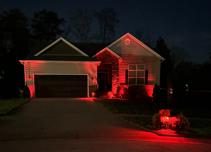 A house at night illuminated with red lights. The house is gray with a garage and a dark driveway.