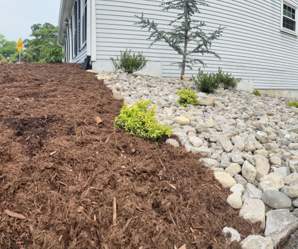 Fresh mulch and river rock landscaping along the side of a white house