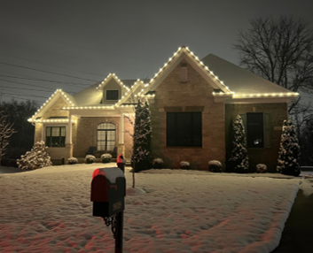 Snow-covered house at night, outlined with warm white holiday lights and a red mailbox in the foreground Snow-covered house at night, outlined with warm white holiday lights and a red mailbox in the foreground