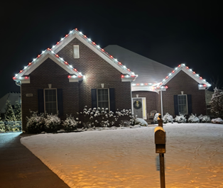 Brick house at night with snow-covered yard and white Christmas lights along the roofline Brick house at night with snow-covered yard and white Christmas lights along the roofline