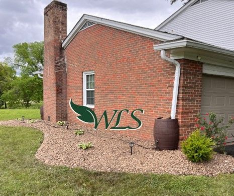 Red brick house with a barrel-shaped rain barrel next to it. A chimney is on the left, and the building has a small window.