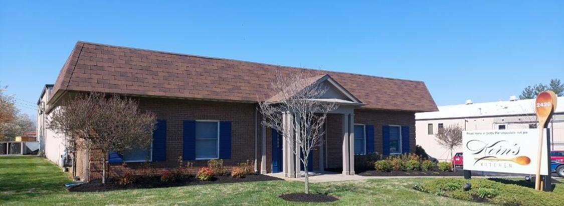 A brick building with blue shutters, brown roof, and a sign for