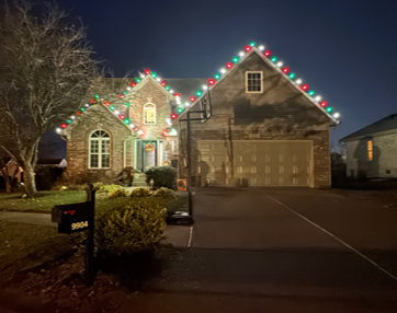 House at night outlined with red and green holiday lights, with a lit driveway and mailbox in front.