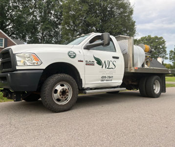 White Ram pickup truck with a flatbed, parked on a street. The truck has a tank and WCS logo on the side.