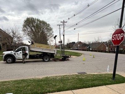 A city truck is parked near a utility pole and stop sign. A worker stands near the truck.