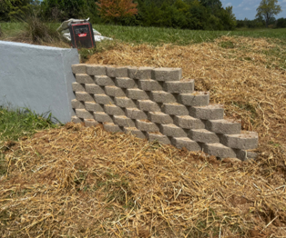 Stacked concrete blocks forming steps beside a white wall in a straw-covered field Stacked concrete blocks forming steps beside a white wall in a straw-covered field