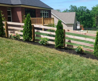 Wooden fence with shrubs along a grassy yard beside a brick house on a sunny day Wooden fence with shrubs along a grassy yard beside a brick house on a sunny day
