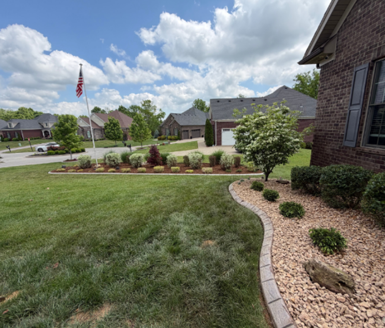 Landscaping services with a manicured lawn and stone-edged rock bed with trimmed shrubs.