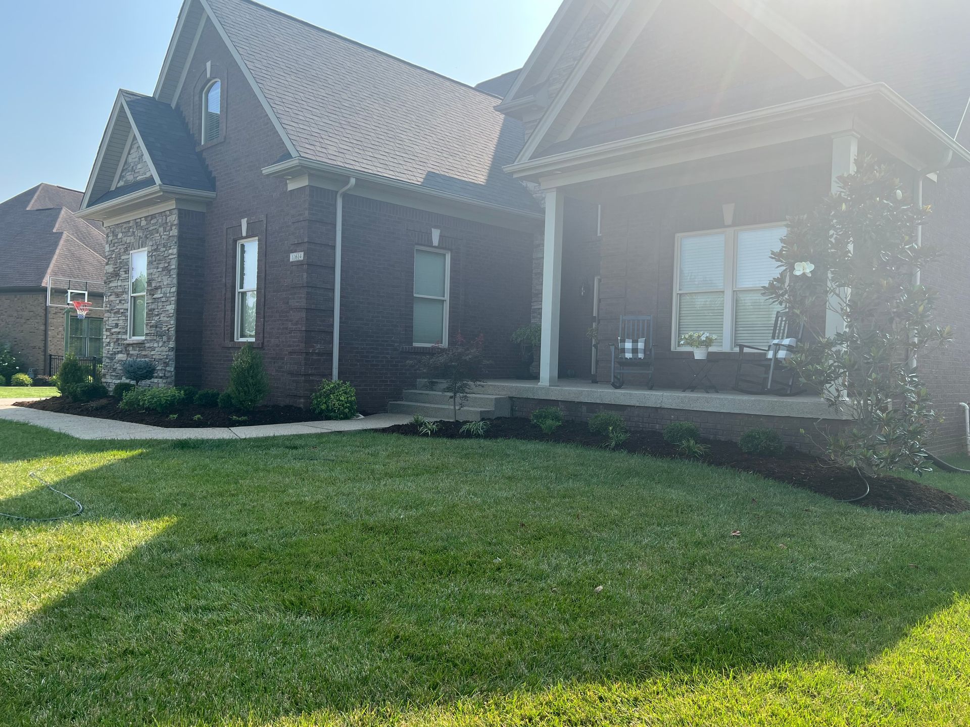 A brick house with a well-maintained lawn and landscaping. The sun shines brightly on the exterior.
