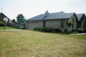 Suburban brick house with a large sloped lawn and a driveway under a clear sky
