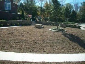 Landscaped front yard with newly mulched bed, rocks, shrubs, and a white sidewalk curb.