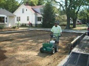Worker using a green machine to maintain a lawn beside a house and sidewalk under trees