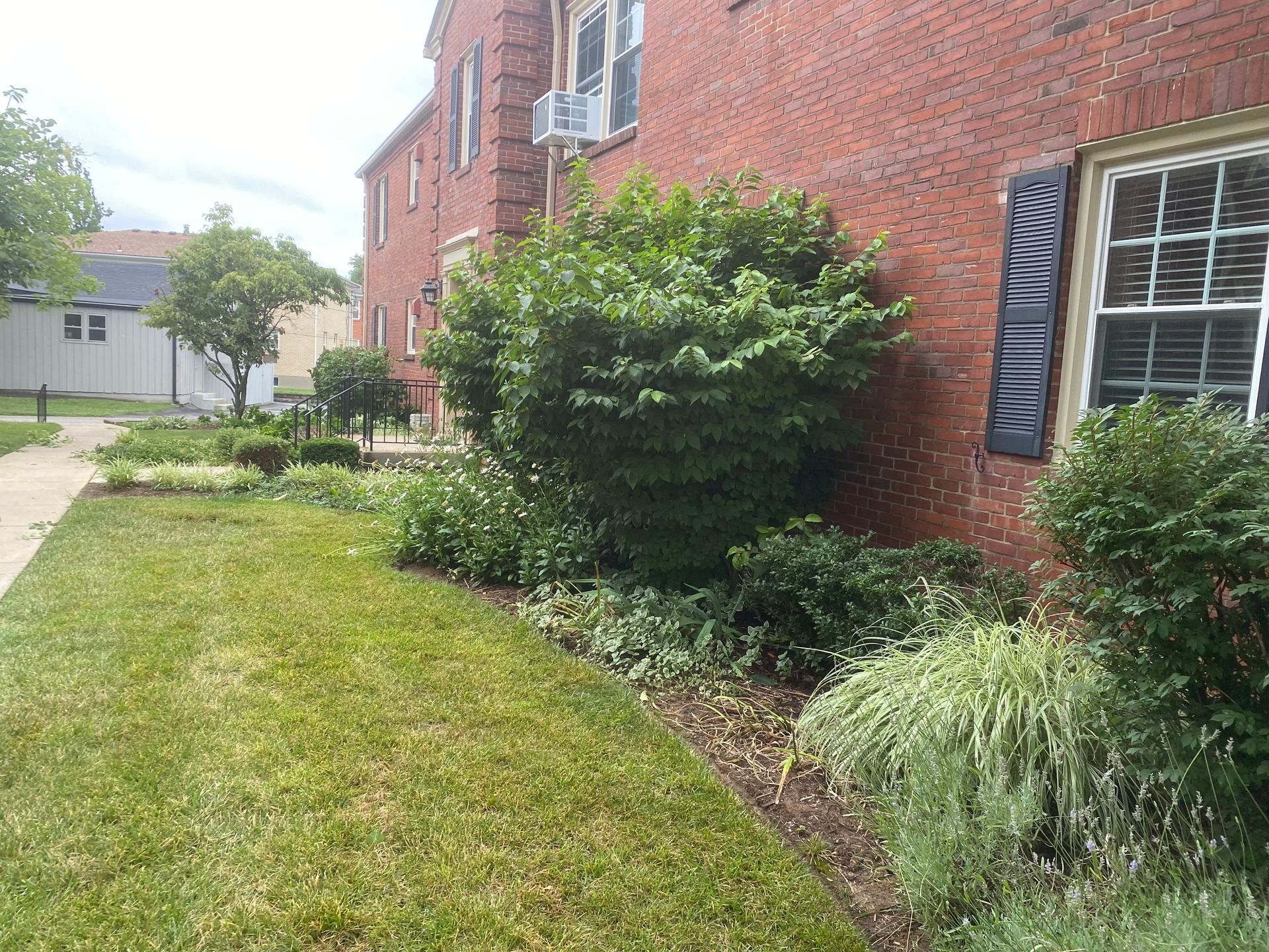 Lush green landscaping borders a red brick building with dark shutters. A sidewalk runs along the grass.