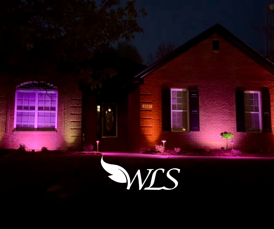 A house exterior illuminated with pink and orange spotlights at night. One window glows bright pink.