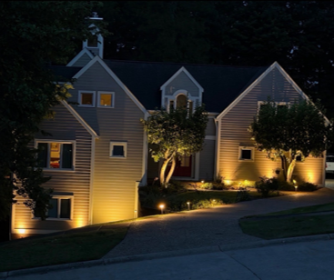 Nighttime view of a row of houses with lit windows and warm landscape lighting along a sloped driveway. Nighttime view of a row of houses with lit windows and warm landscape lighting along a sloped driveway.