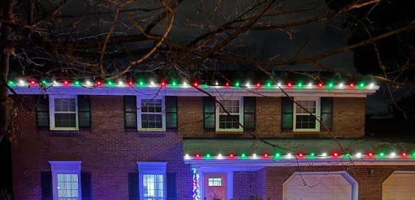 Brick house at night outlined with colorful Christmas lights and a glowing garage door with red bows