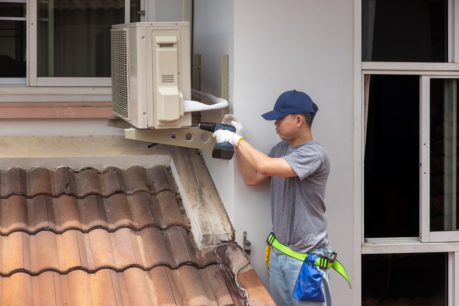 A person in a blue cap installing an outdoor air conditioning unit with a power drill.