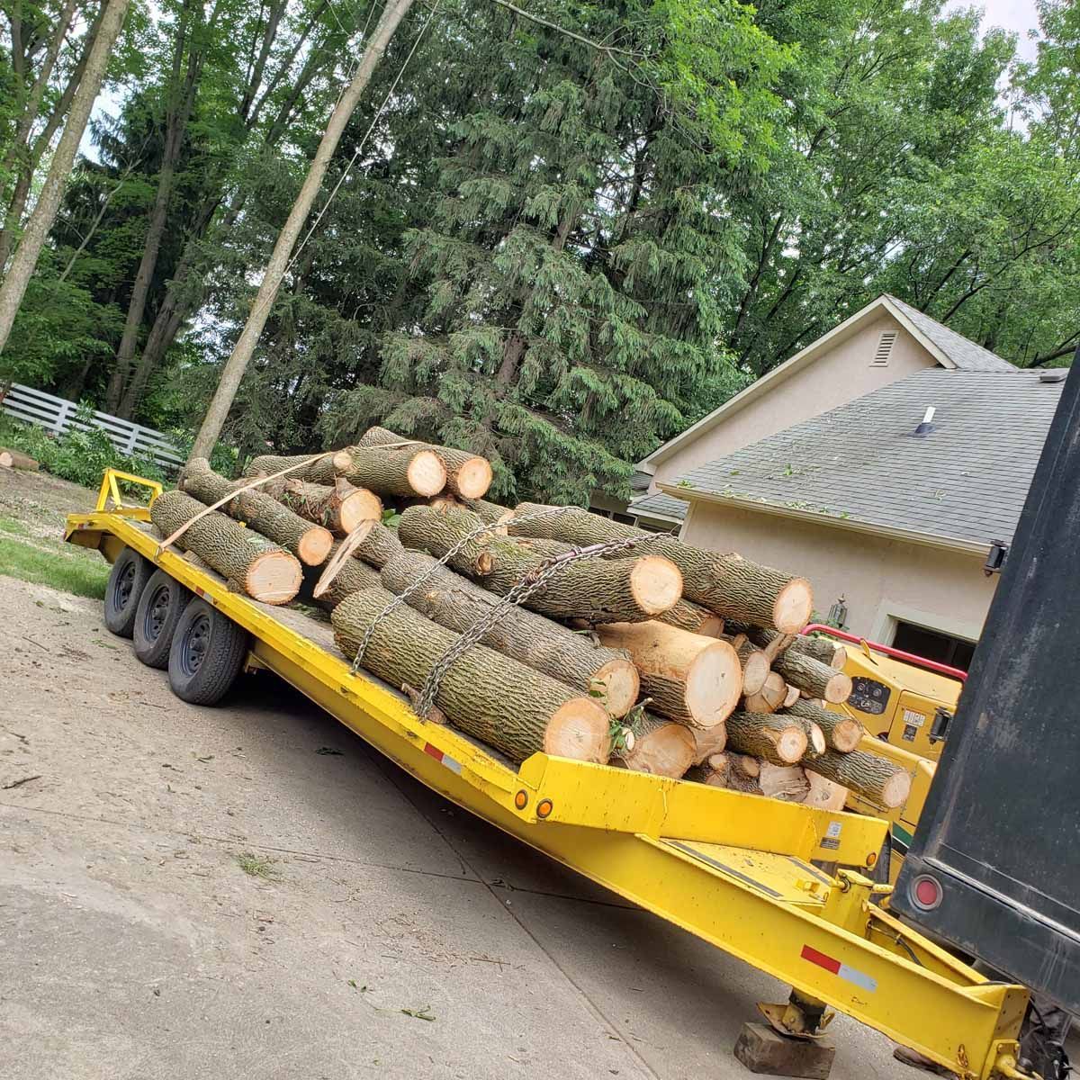 A trailer filled with logs is parked in front of a house.