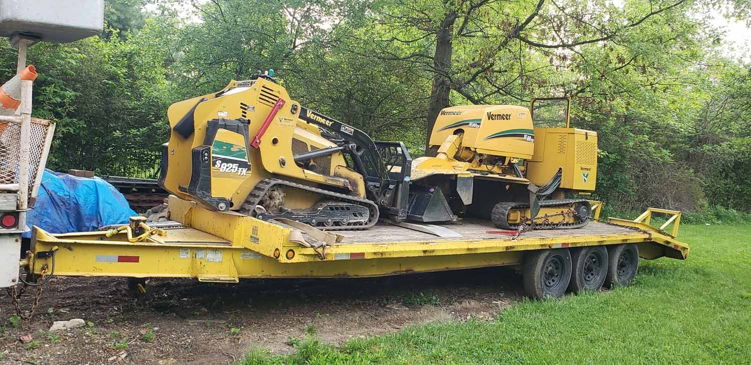 A yellow trailer with two tractors on it is parked in a grassy field.