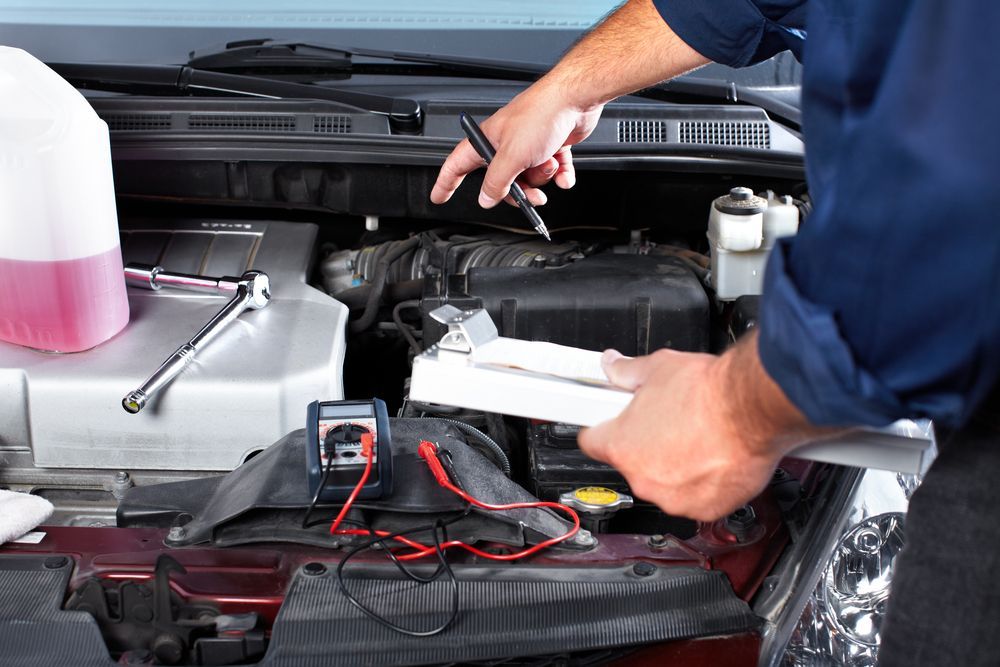 Mechanic working on car engine, holding clipboard and pen, with tools and fluid — Prime Mobile Mechanics in Varsity Lakes, QLD