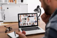 Um homem está sentado em uma mesa usando um laptop para fazer uma chamada de vídeo com um grupo de pessoas.