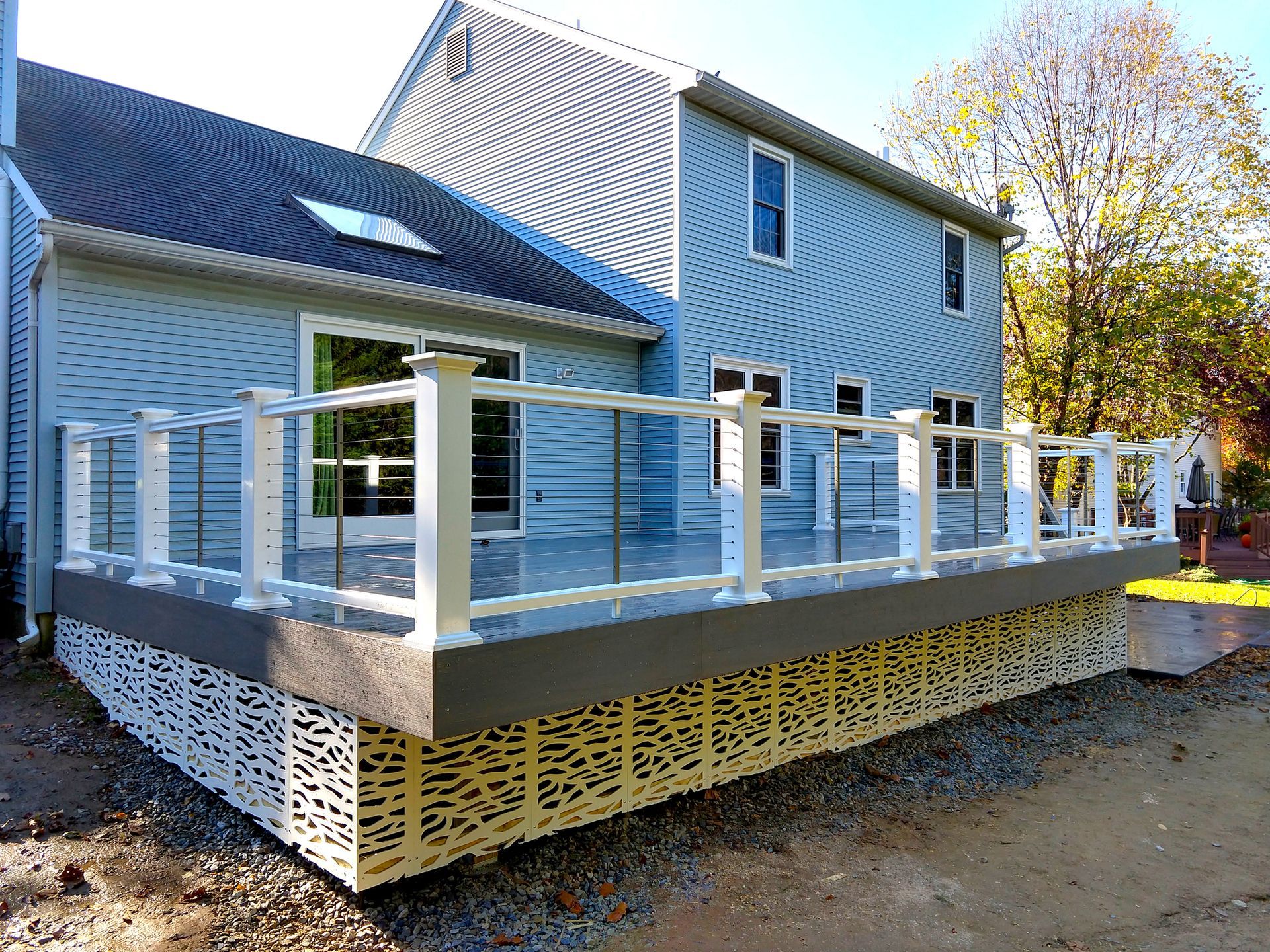 New outdoor deck with white railing, gray composite deck, and patterned skirting, attached to a light blue house.