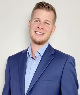 A man in a blue suit and blue shirt is smiling for the camera.