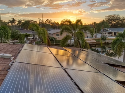 A row of solar panels on a roof with a sunset in the background.