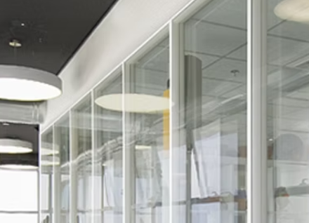 A long hallway with a lot of glass walls and ceiling lights.