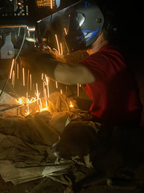 Person welding metal in a dim workshop, sparks flying from the workpiece.