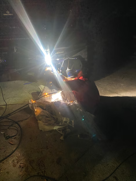 Person welding metal outdoors at night, bright sparks and strong light illuminating the scene