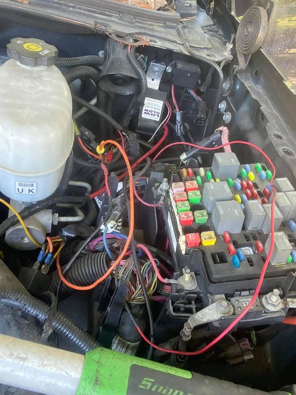 Engine compartment with exposed wires, relays, and fuse box. Red, orange, and black wiring is prominent.