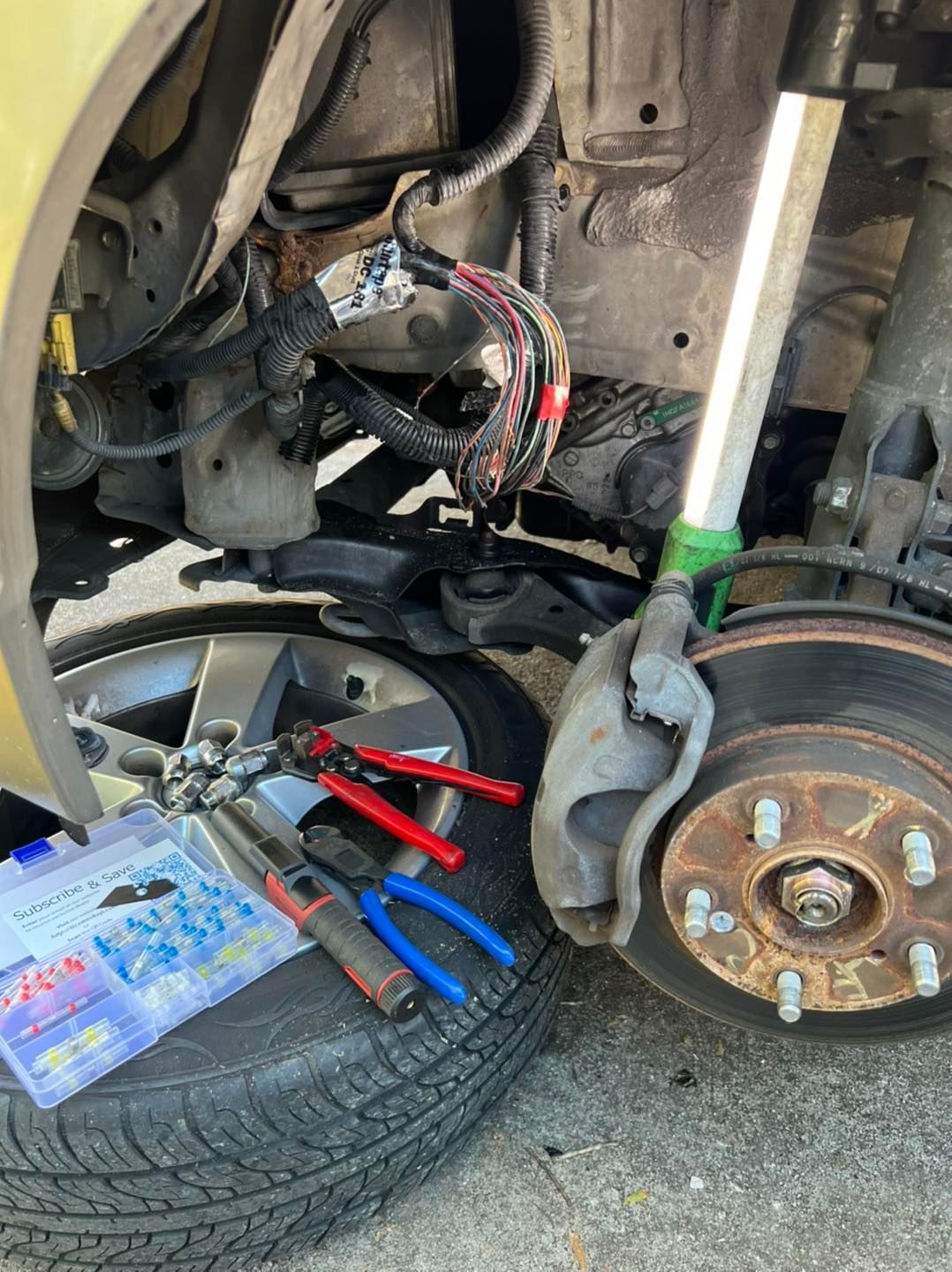 Car repair: wiring and tools are on a tire near the front wheel.