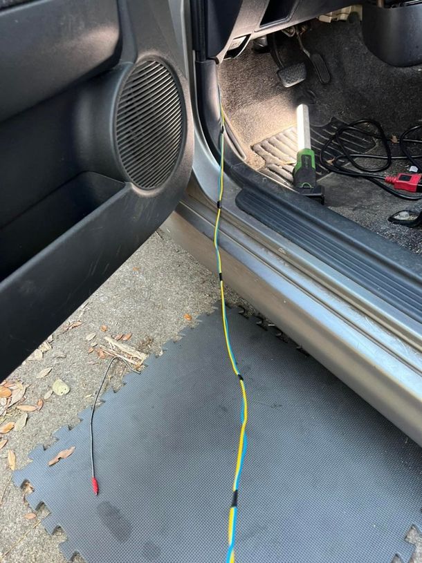 Car door open, wires exposed running from interior to outside. Yellow and blue wires taped together.