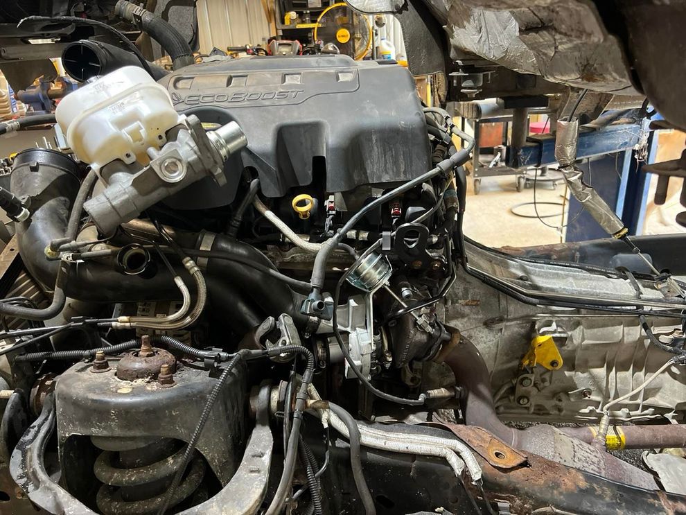 Engine of a vehicle, in a workshop, with various parts and wires visible.