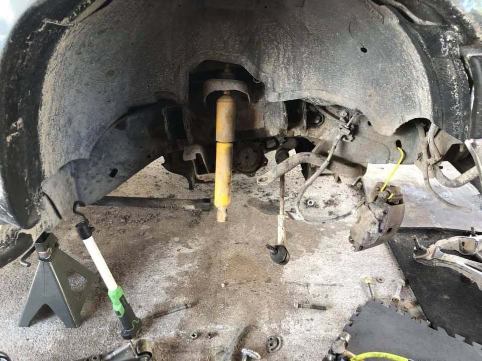 Car suspension components being worked on, including a shock absorber, against a dirty wheel well.
