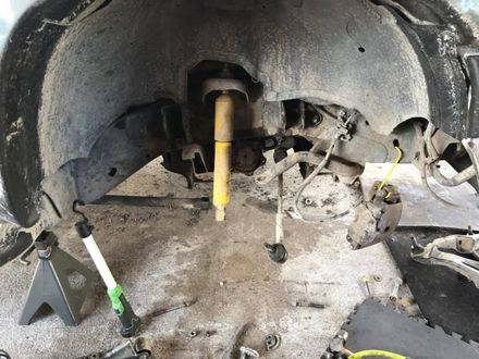 Car wheel well with removed suspension components, including a yellow shock absorber, on jack stands.