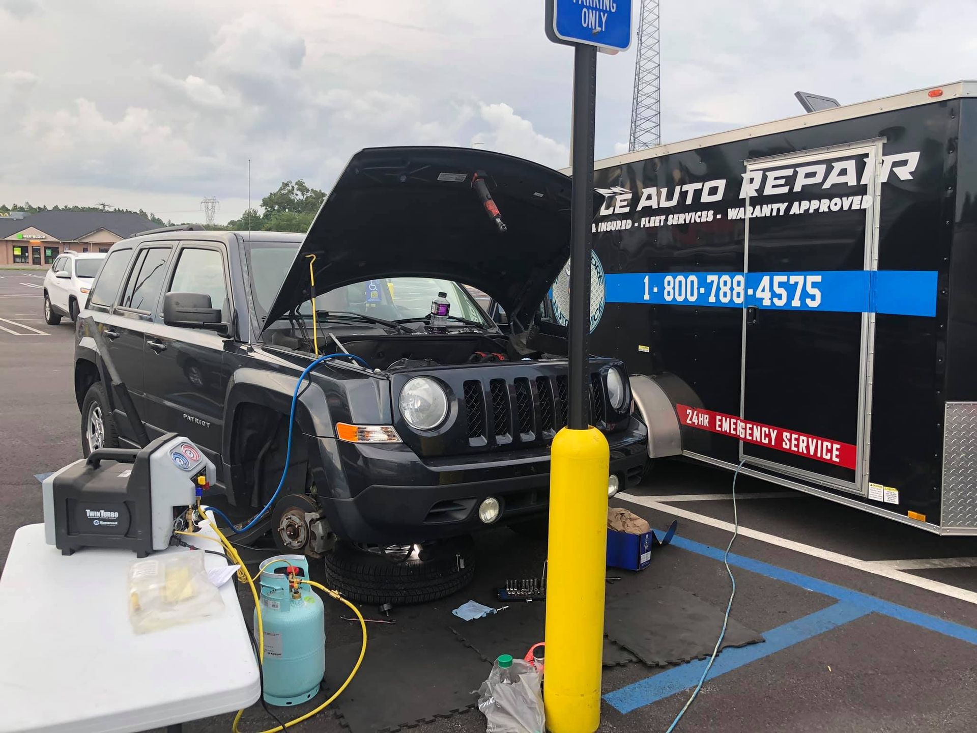 A black Jeep being serviced by a mobile auto repair business; hood open, tires removed.