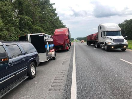 Trucks and trailer stopped on highway shoulder under cloudy skies.