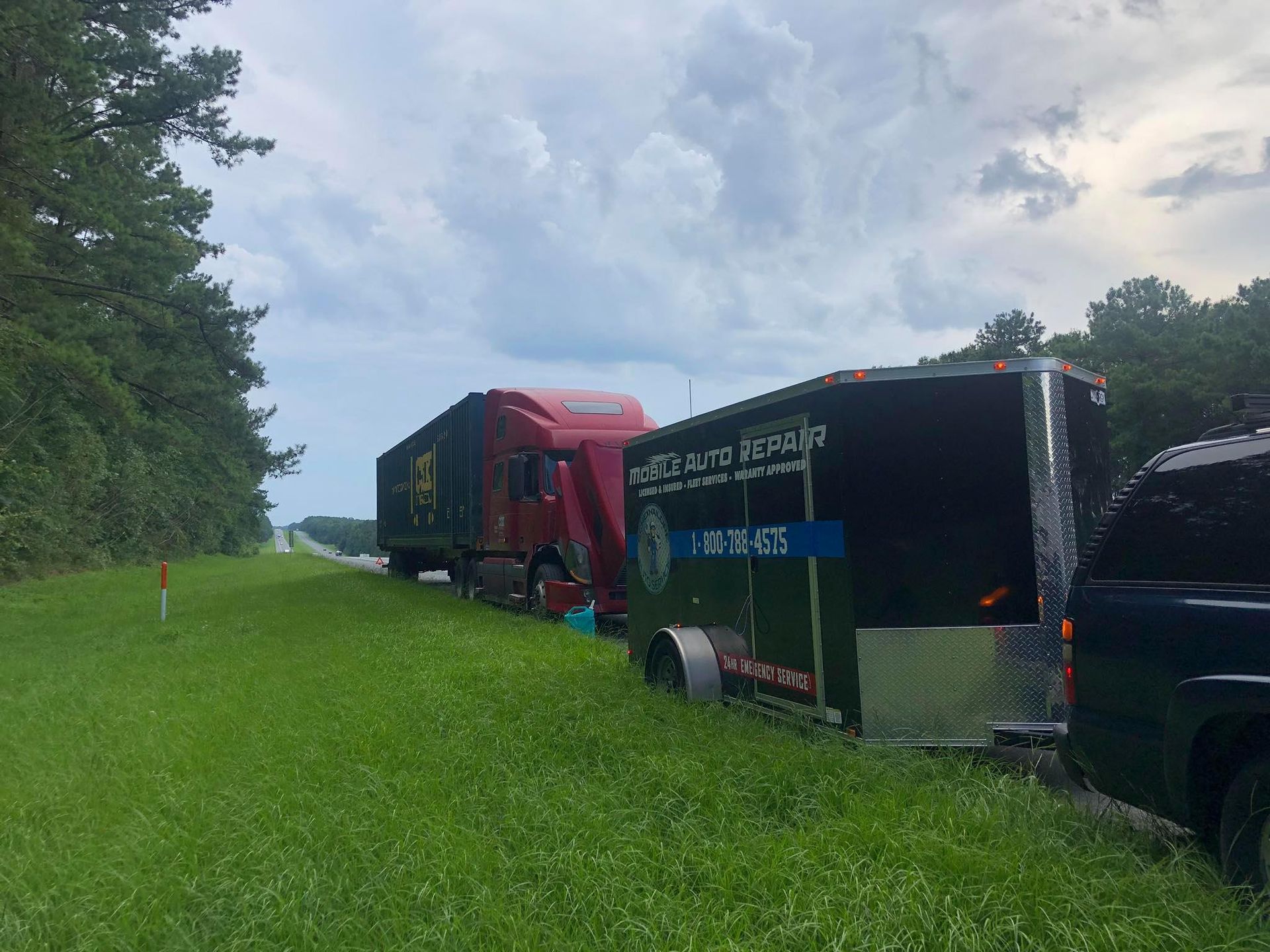 A tow truck pulling a semi-truck on a grassy shoulder of a road.