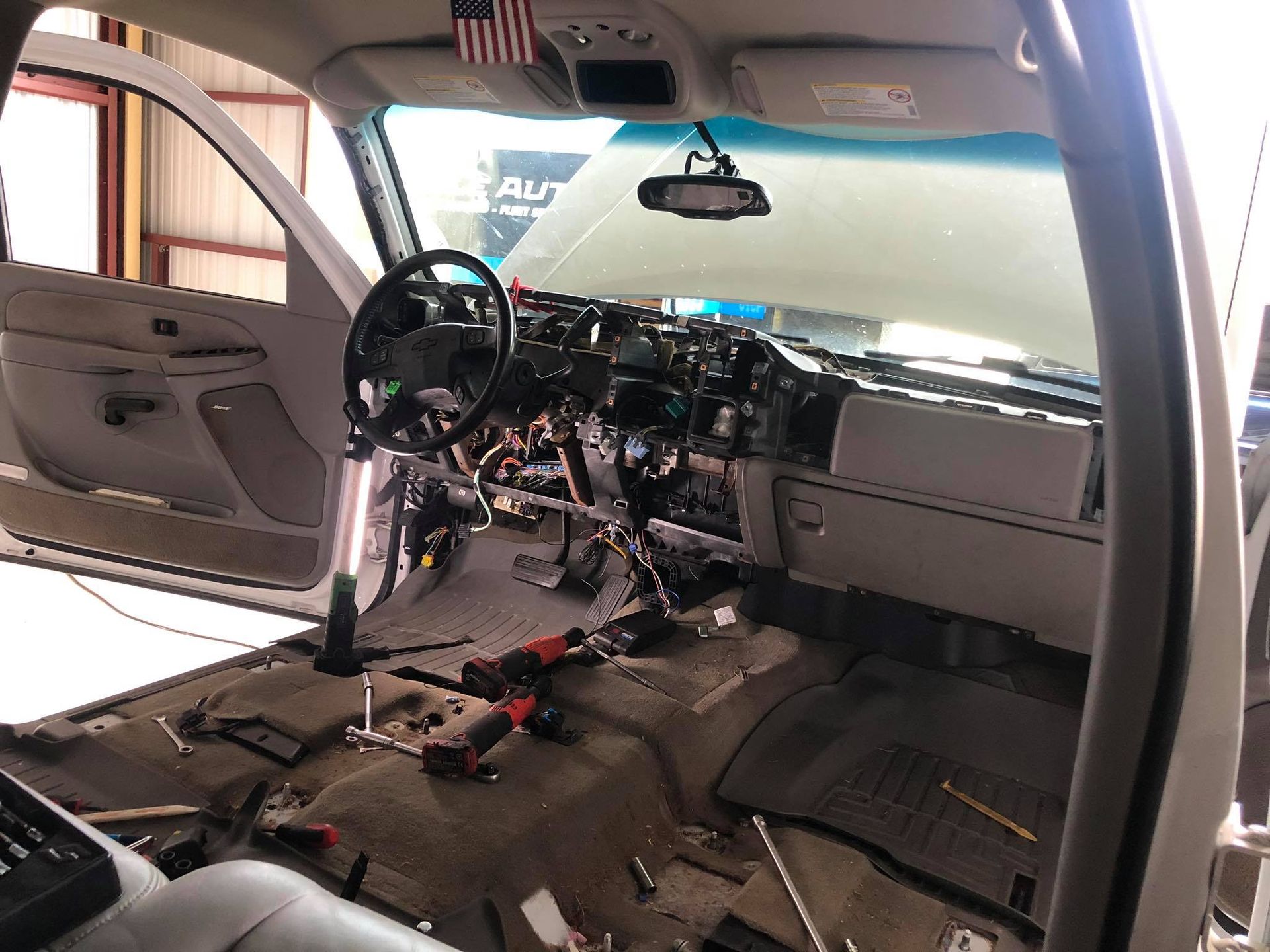 Interior of a vehicle with dashboard disassembled; tools and wiring visible. American flag hanging.