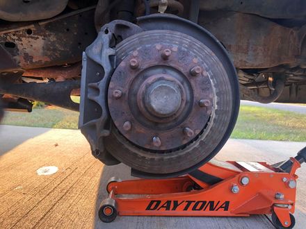 Rusty car brake rotor with caliper; orange Daytona jack supporting it.