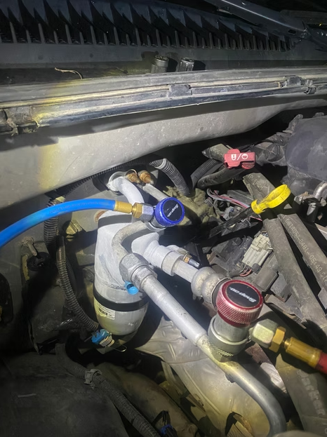 Close-up of car engine bay with hoses, coolant reservoir, and colored valve caps.