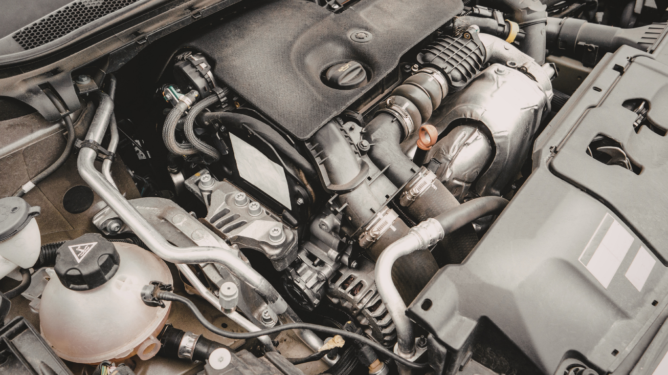 Car engine bay with various components, including hoses, a coolant reservoir, and the engine itself.