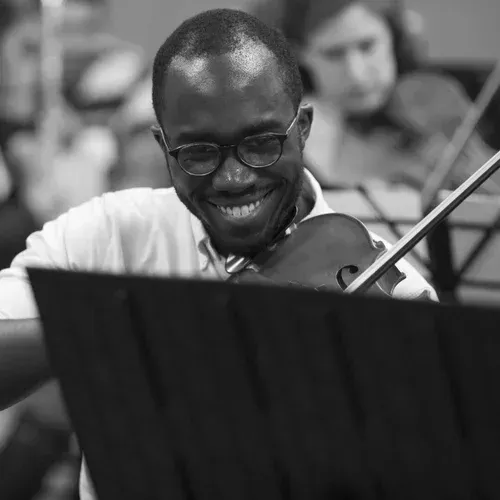 Smiling musician playing violin in an orchestra, viewed over a black music stand