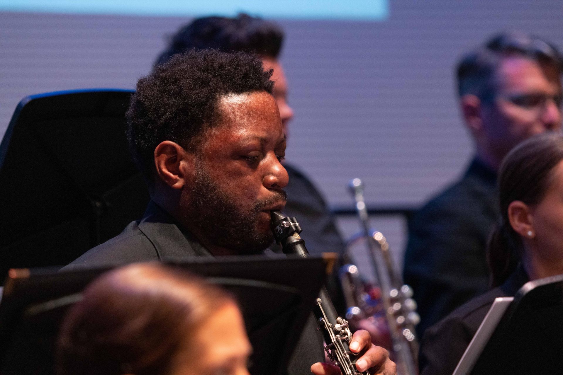 Musician playing clarinet in an orchestra with blurred seated performers in the background